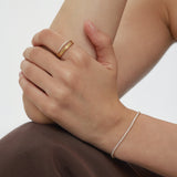 A close-up of a person’s hands resting on their knee, wearing a gold ring and the Lumi Tennis Bracelet in Gold with cubic zirconia, against soft brown fabric and a neutral background.