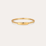 The Lya Horizontal Bar Stacking Ring in Gold features a sleek rectangular plate atop a twisted band, perfect for wearing solo or stacked with other rings. Shown against a simple light background.