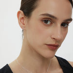 Woman wearing a delicate necklace with a silver pendant on a plain background