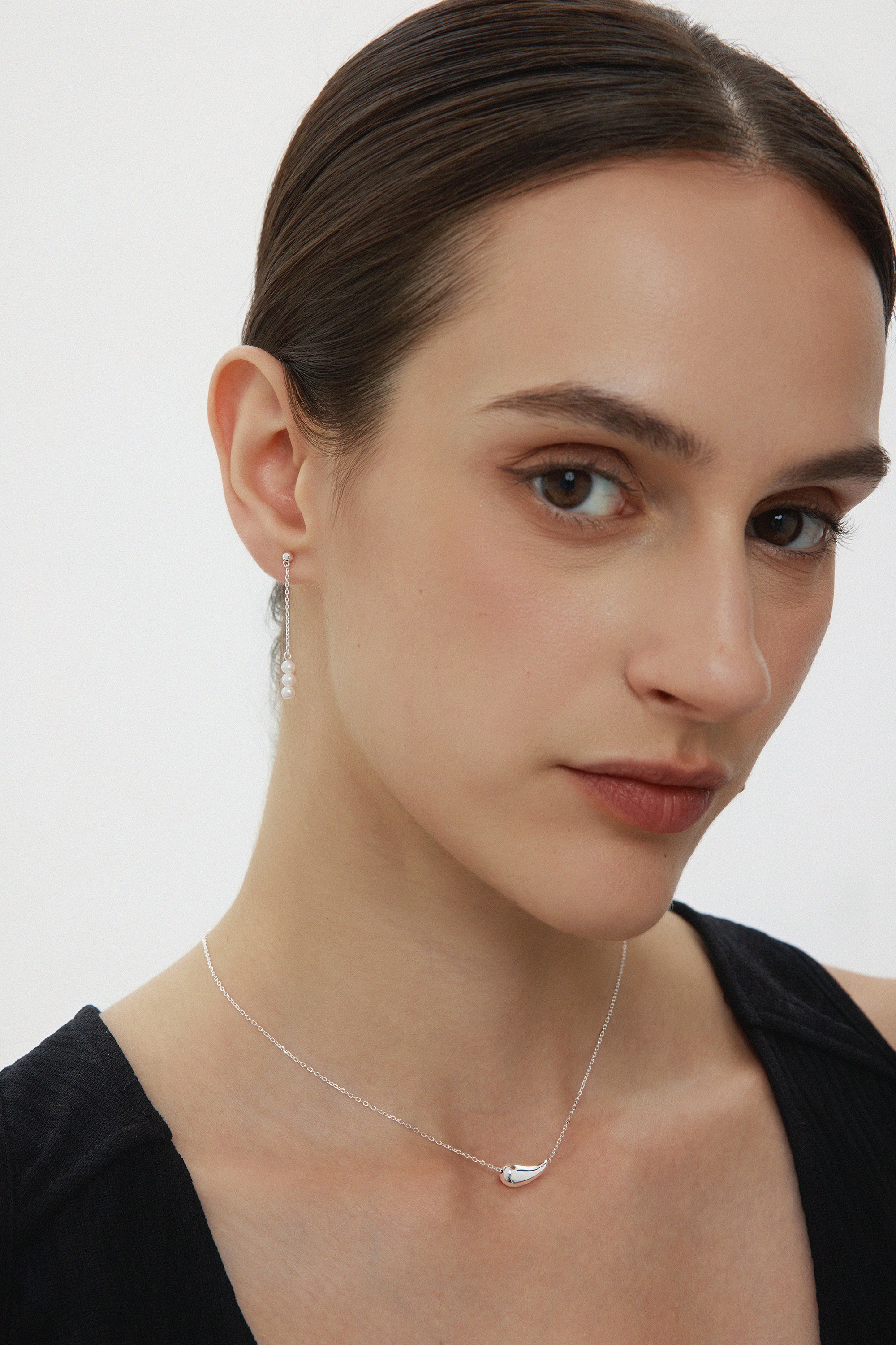 Woman wearing a delicate necklace with a silver pendant on a plain background