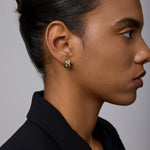 A woman with dark hair in a neat bun wears a black blazer and showcases the Mia Two-tone Mixed Metal Hoops. She appears in profile against a plain, light gray background.