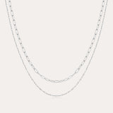 The Mini Paperclip Double Chain Necklace in Silver features two sterling silver layers: an upper chain with elongated oval links and a lower chain with smaller, closely connected links for a simple, elegant look.