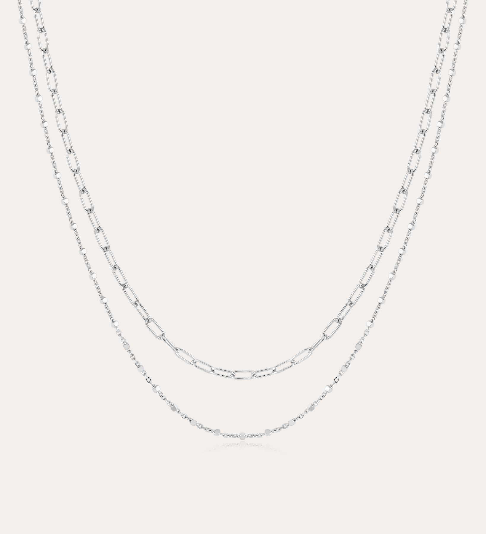 The Mini Paperclip Double Chain Necklace in Silver features two sterling silver layers: an upper chain with elongated oval links and a lower chain with smaller, closely connected links for a simple, elegant look.