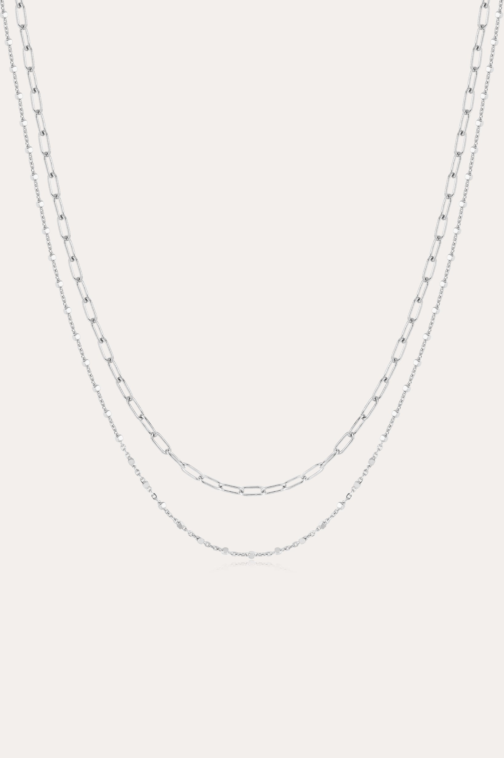 The Mini Paperclip Double Chain Necklace in Silver features two sterling silver layers: an upper chain with elongated oval links and a lower chain with smaller, closely connected links for a simple, elegant look.