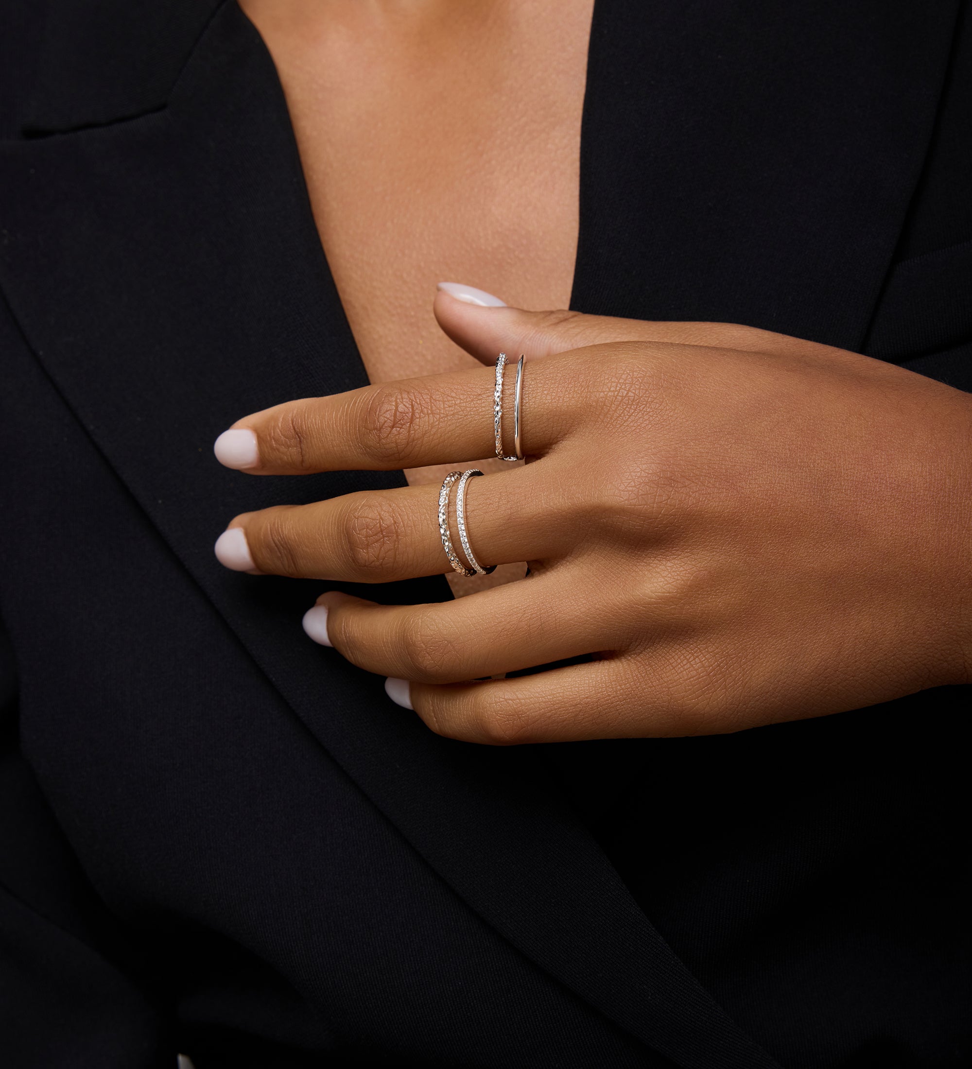 A person with medium skin tone, neatly manicured nails, and light polish wears a black blazer and showcases two delicate sterling silver rings, including the Molten Crystal Double Band Ring in Silver set with small diamonds.