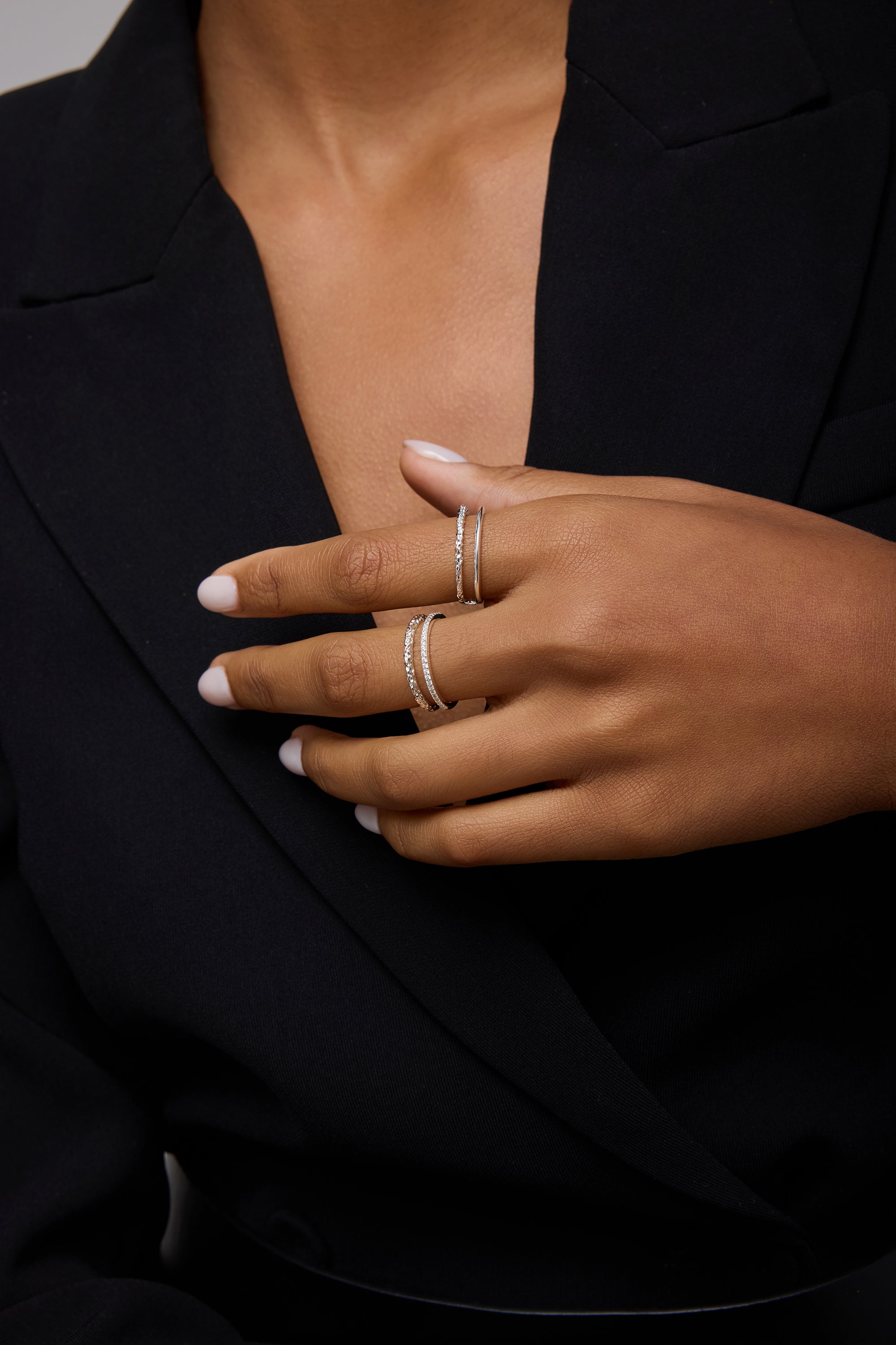 A person with medium skin tone, neatly manicured nails, and light polish wears a black blazer and showcases two delicate sterling silver rings, including the Molten Crystal Double Band Ring in Silver set with small diamonds.