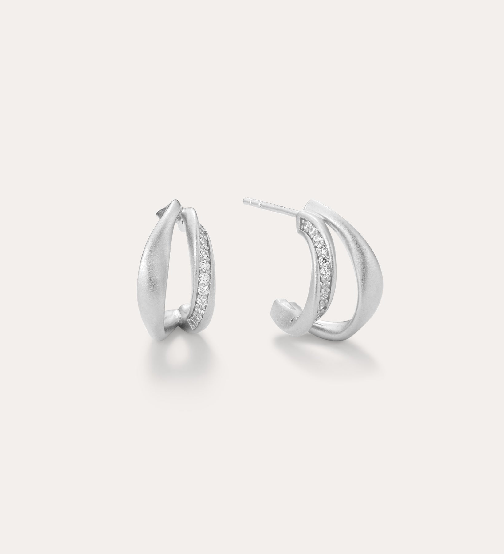Nadine Pavé Twisted Stud Earrings in Silver feature lightweight, asymmetrical silver hoops with a row of sparkling stones along the inner curve, displayed on a plain white background.