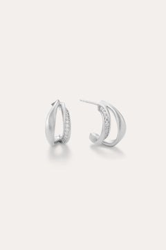 Nadine Pavé Twisted Stud Earrings in Silver feature lightweight, asymmetrical silver hoops with a row of sparkling stones along the inner curve, displayed on a plain white background.