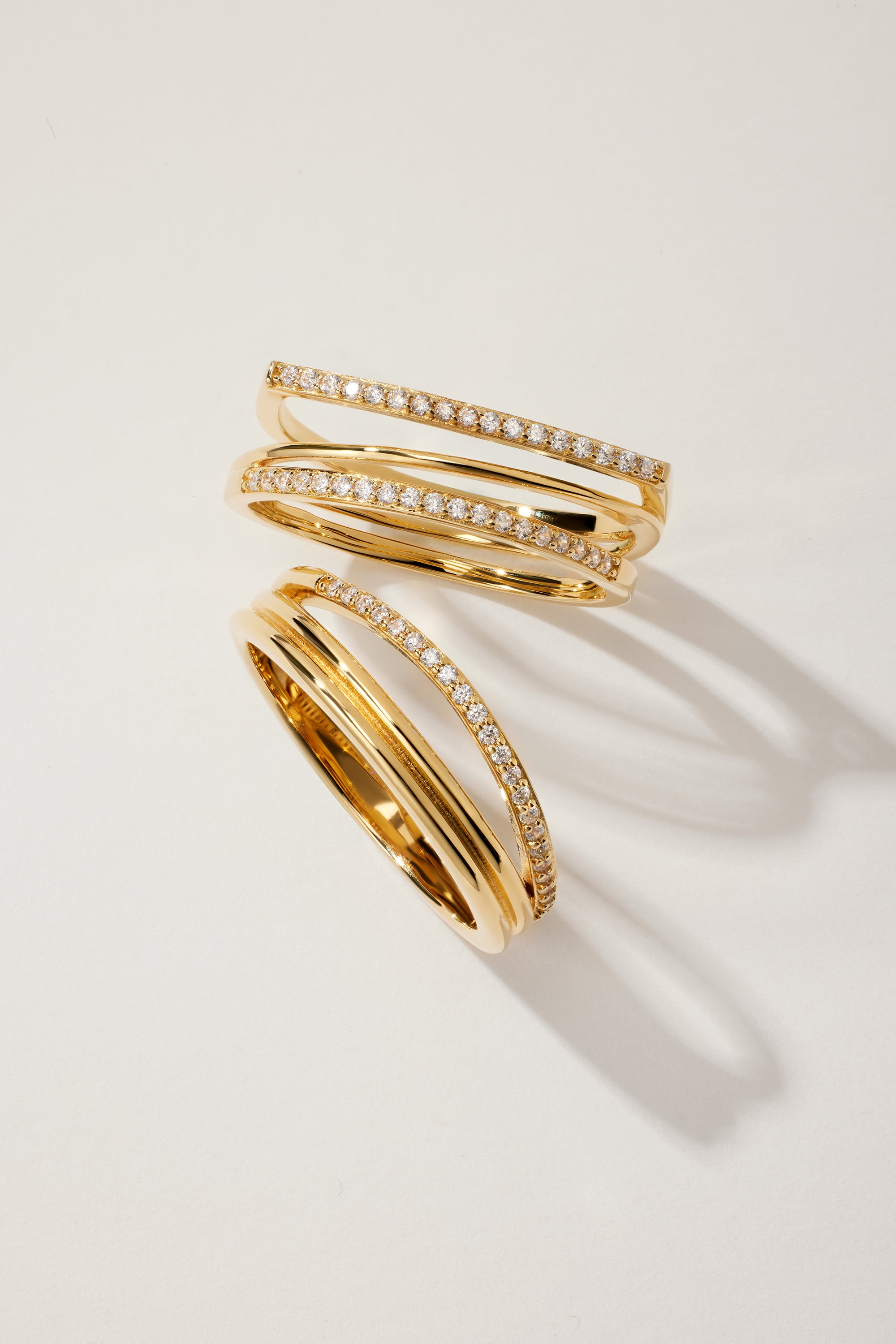 The Noor Pavé Triple Band Ring in Gold features overlapping pavé bands, each set with a row of sparkling diamonds, displayed on a light background with soft shadows.