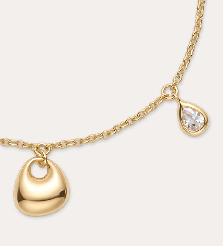 The Nora Double Pendant Bracelet in Gold features a small gold heart charm and a teardrop-shaped cubic zirconia, finished with an adjustable clasp and extension chain.