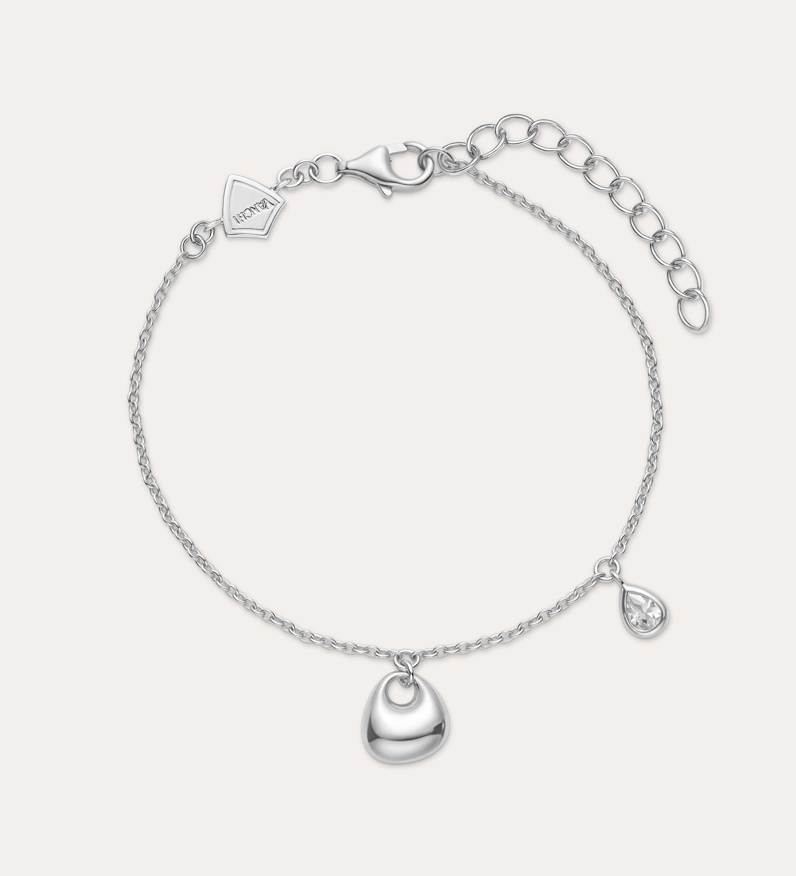 The Nora Double Pendant Bracelet in Silver features a polished heart charm at the center and a small teardrop pendant, both accented with cubic zirconia, plus an adjustable clasp and logo tag near the fastening.