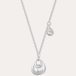 The Nora Double Pendant Necklace in Silver features a fine chain with a shiny sculptural pendant and a separate tiny teardrop charm set with a clear cubic zirconia, displayed against a plain background.