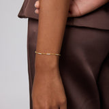 A person in a brown satin outfit rests their left arm by their side, showing off the Pia Crystal Link Bracelet in Gold on their wrist against a plain, neutral background.