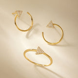 Three Reneé Triangle Linear Hoop Stud Earrings in Gold, each adorned with a diamond-studded triangle, are artfully arranged on a beige background with soft shadows.