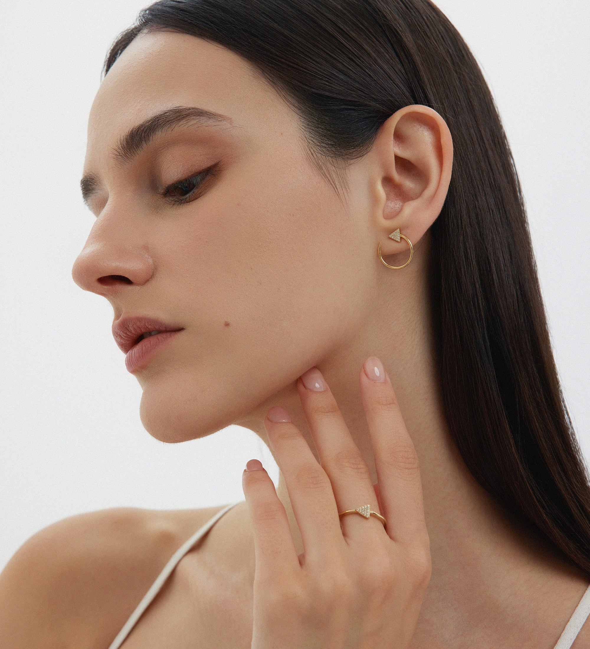 Woman wearing gold earrings and a ring, with a neutral background