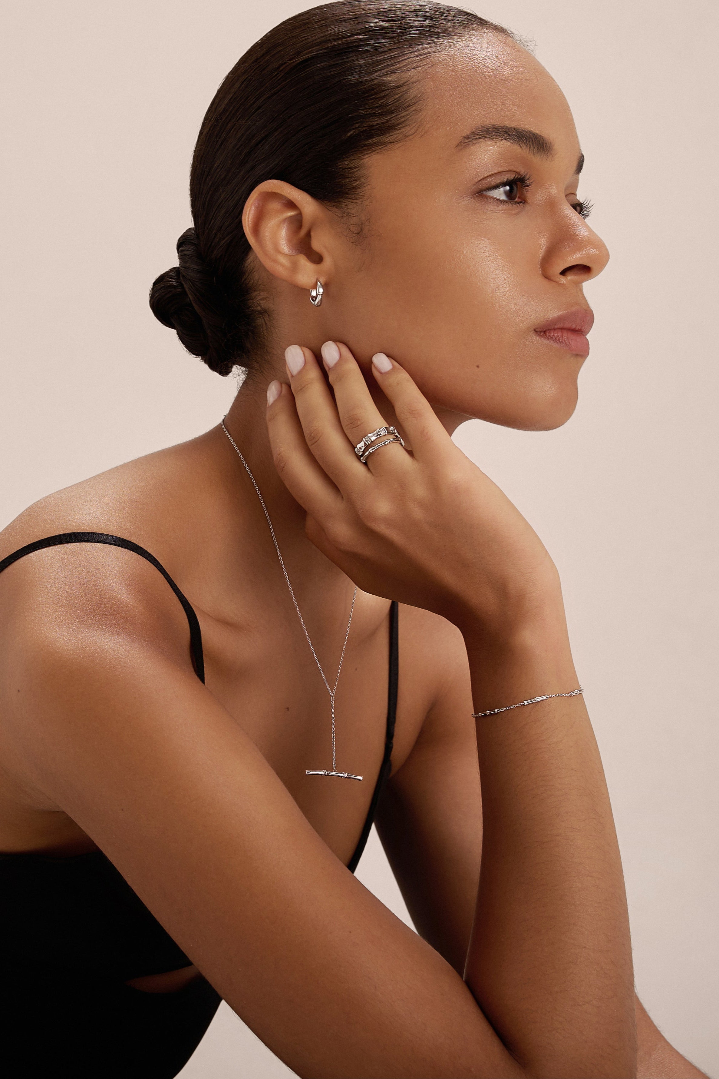A woman with slicked-back hair wears a black sleeveless top and minimal jewelry, including the Bamboo Ring in Silver, as she thoughtfully poses with her hand on her chin against a plain background.