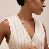 A woman with dark hair in a low bun models the Gisèle Cuban Link Bar Bracelet in Silver, paired with minimalist silver jewelry—hoop earrings, a bar necklace, and a simple ring—while wearing a cream pinstriped sleeveless top.