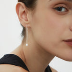 Close-up of a woman with brown hair in a black top, wearing Eira Pearl Drop Threader Earrings in Silver. She faces slightly right, highlighting her cheek, lips, and the elegant shimmer of her pearl drop earrings.