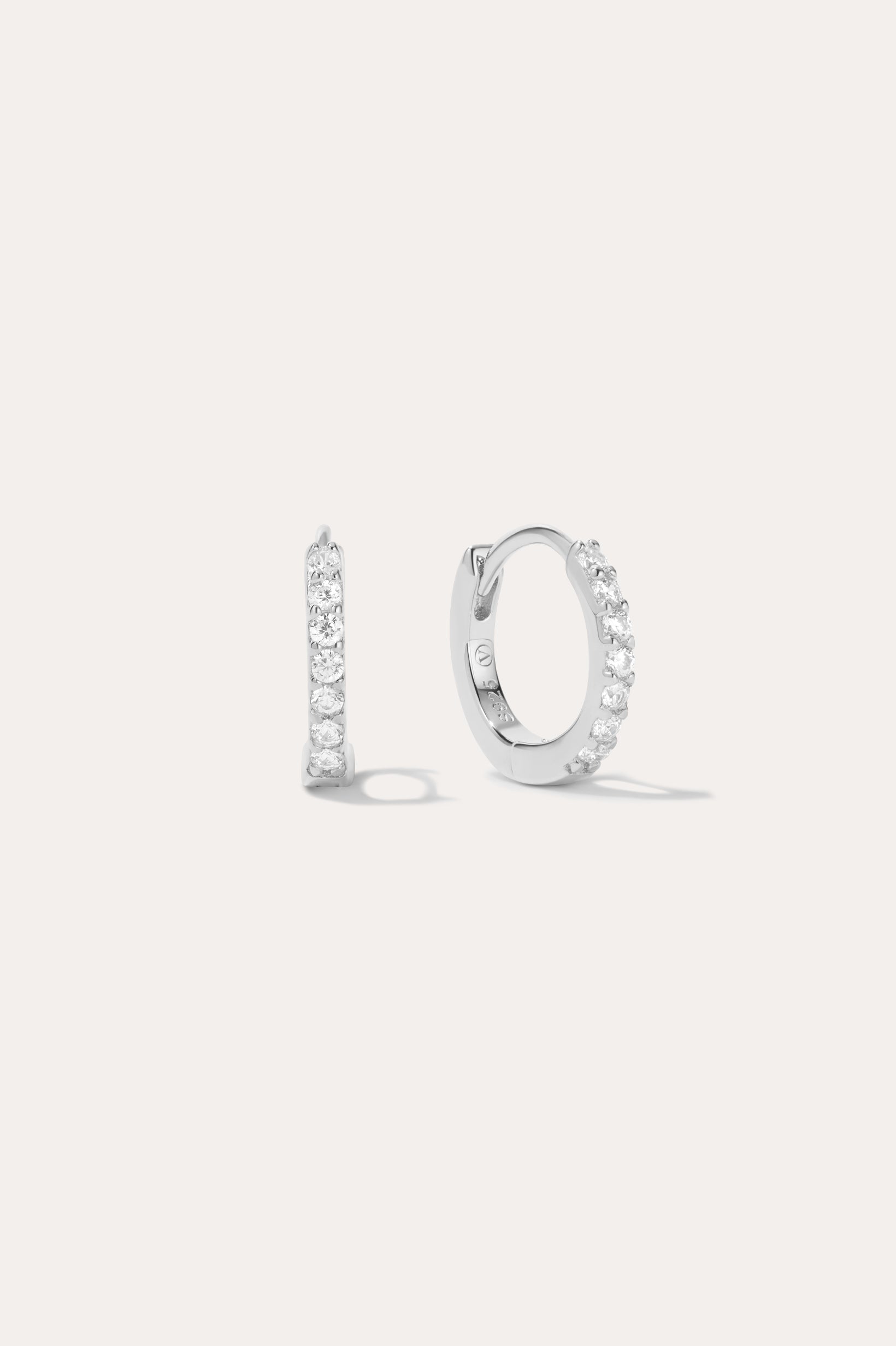 The Kiki Crystal Huggie Earrings in Sterling Silver feature a sparkling row of white gemstones. Shown facing forward and from the side, they are versatile everyday essentials for any ear piercing.