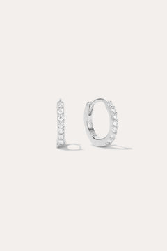 The Kiki Crystal Huggie Earrings in Sterling Silver feature a sparkling row of white gemstones. Shown facing forward and from the side, they are versatile everyday essentials for any ear piercing.