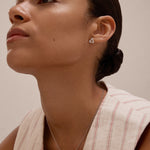 A woman with slicked-back hair wears a sleeveless, cream top with red stripes and the Colette Droop Link Studs in Silver, paired with a simple bar necklace. She gazes slightly upward against a neutral background.