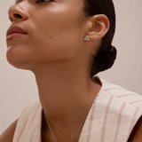 A woman with slicked-back hair wears a sleeveless, cream top with red stripes and the Colette Droop Link Studs in Silver, paired with a simple bar necklace. She gazes slightly upward against a neutral background.