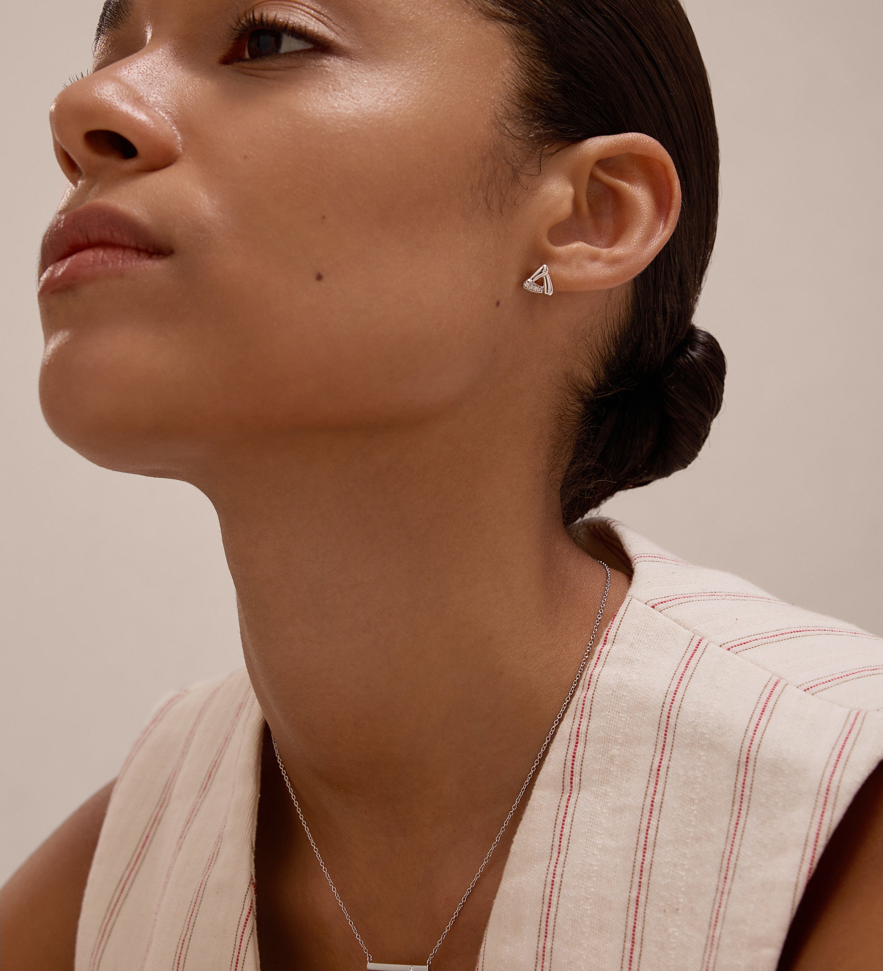 A woman with slicked-back hair wears a sleeveless, cream top with red stripes and the Colette Droop Link Studs in Silver, paired with a simple bar necklace. She gazes slightly upward against a neutral background.