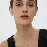 Woman wearing a delicate necklace with a plain background