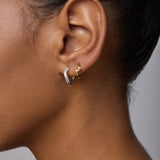 Close-up of a woman’s ear with everyday jewelry: a small gold hoop in the upper lobe and Nori Twisted Hoop Earrings in Silver in the lower lobe. She has smooth brown skin and dark hair pulled back.