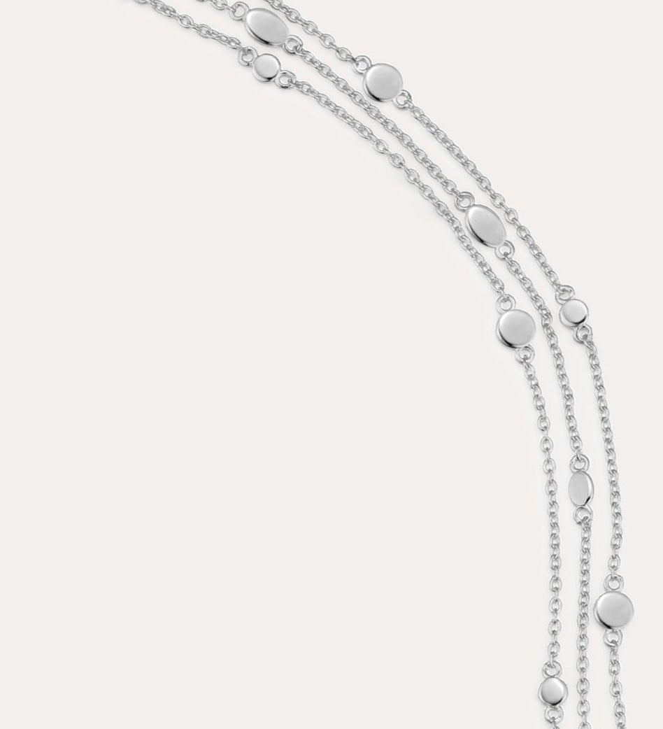 The Simone Triple Chain Layered Bracelet in Silver features three delicate sterling silver chains adorned with small round and oval disc accents, finished with a lobster clasp closure.