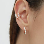 A close-up shows brown hair tucked behind an ear styled with an elegant stack: the Vale Crystal Ear Cuff in Silver featuring sparkling gemstones on the upper ear and a twisted silver hoop earring in the lobe.