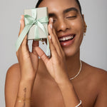 Woman holding a small gift box with a green ribbon against a neutral background