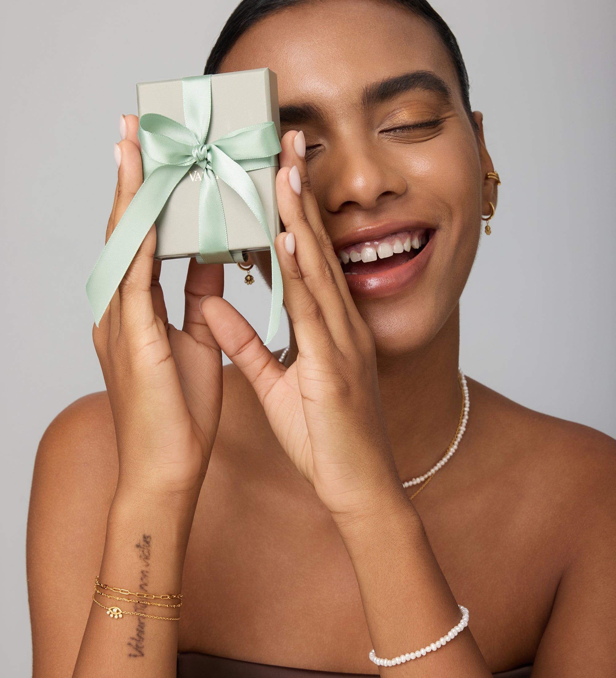 Woman holding a small gift box with a green ribbon against a neutral background