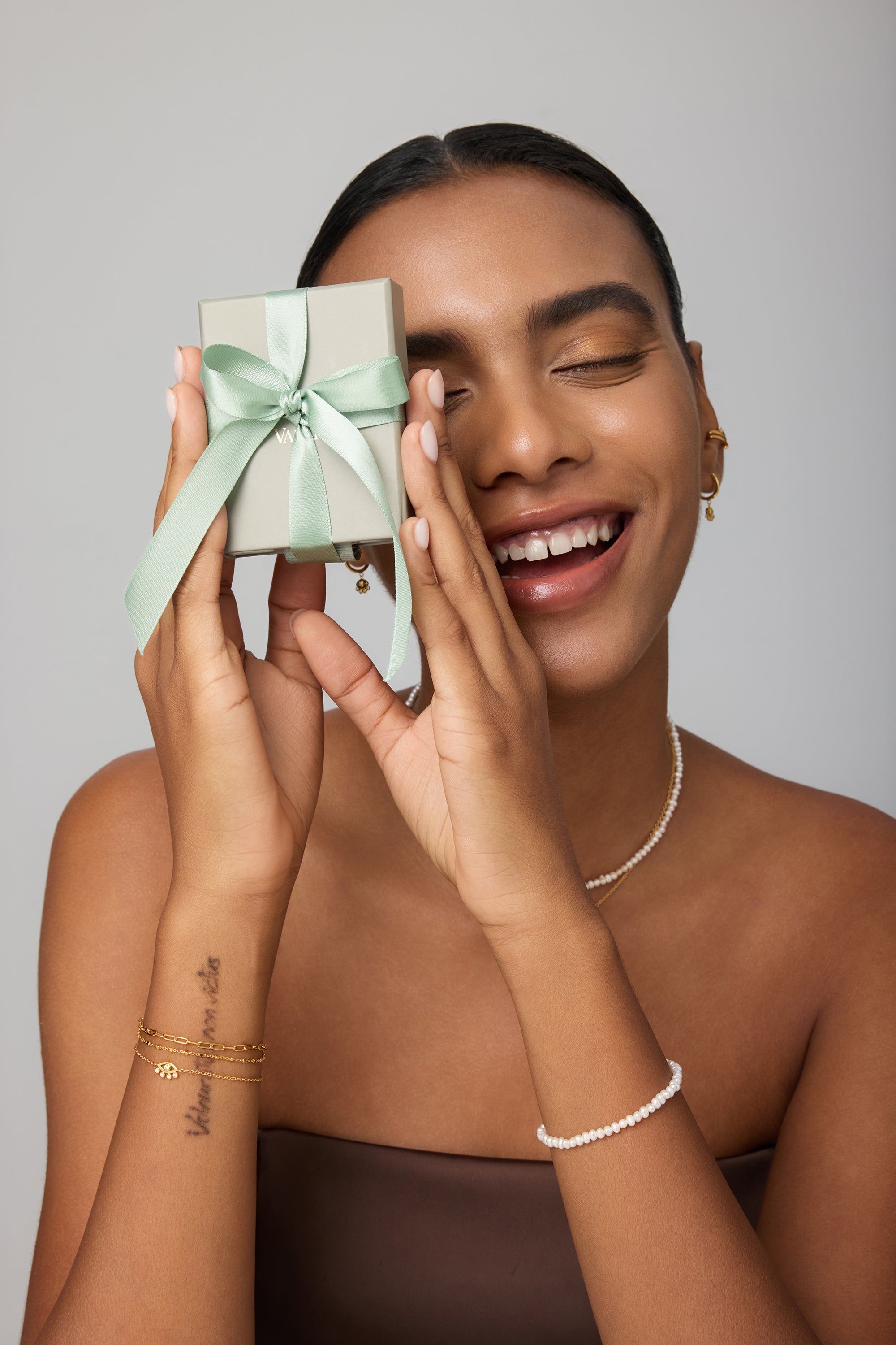 Woman holding a small gift box with a green ribbon against a neutral background