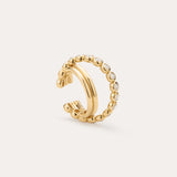 The Vina Crystal Bezel Ear Cuff in Gold features a beaded design with small, round clear cubic zirconia along the outer edge, shown on a light beige background.