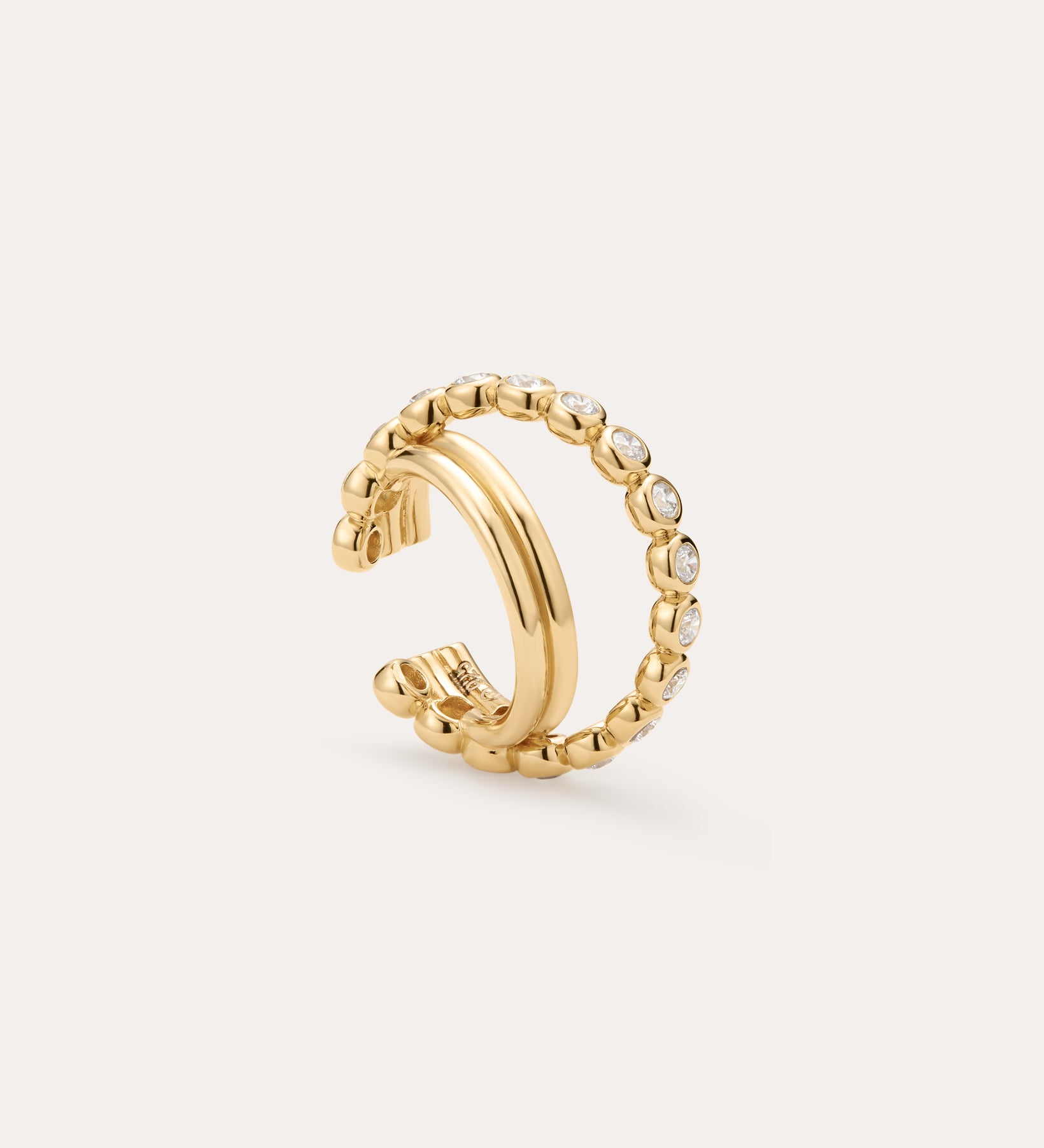 The Vina Crystal Bezel Ear Cuff in Gold features a beaded design with small, round clear cubic zirconia along the outer edge, shown on a light beige background.