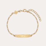 The Viva La Vida Bar Chain Bracelet in Gold features an adjustable clasp, a rectangular plate engraved with VIVA LA VIDA, and a small hexagonal charm near the clasp. Inspired by the classic Viva La Vida necklace; shown on a light beige background.