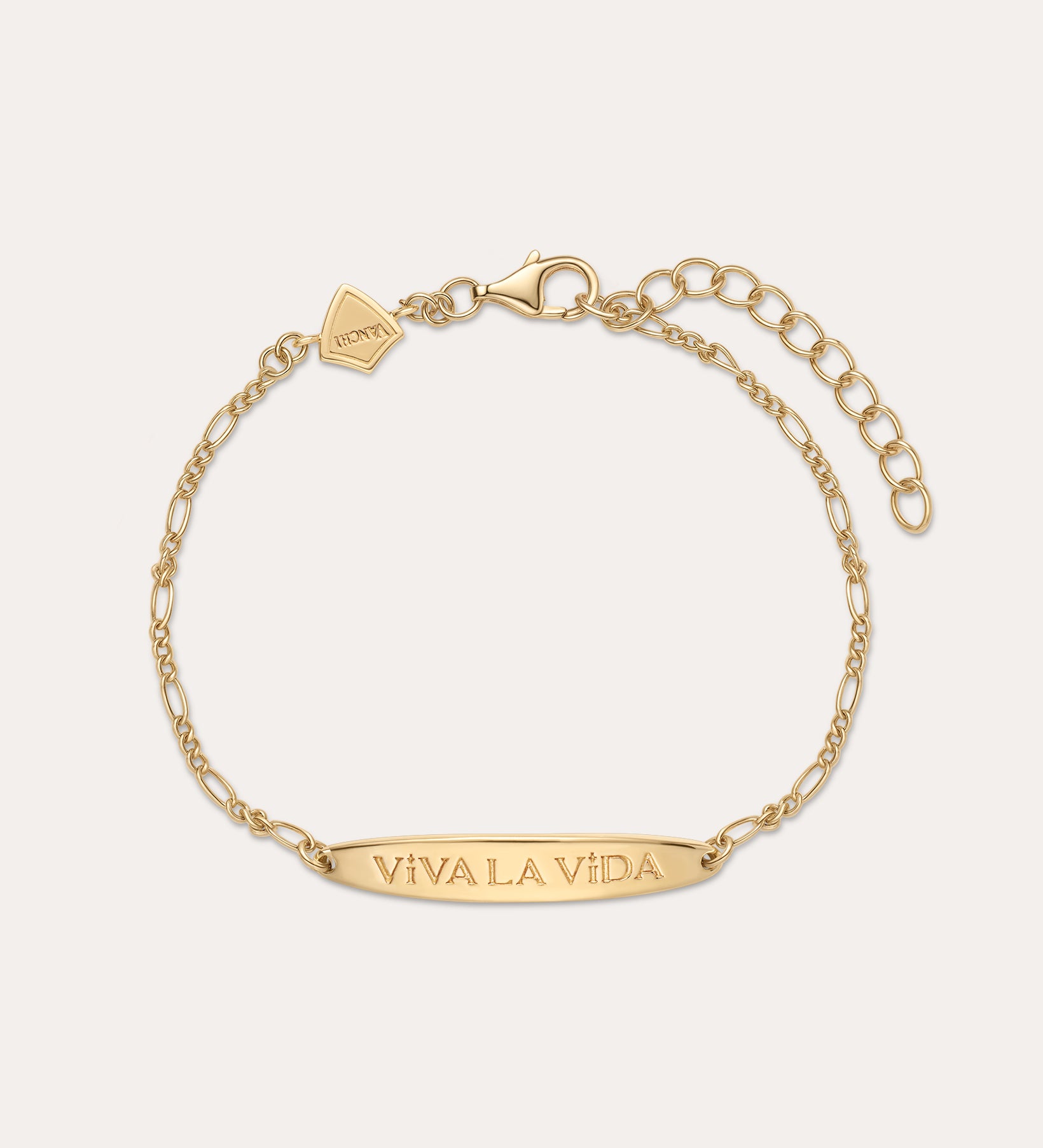 The Viva La Vida Bar Chain Bracelet in Gold features an adjustable clasp, a rectangular plate engraved with VIVA LA VIDA, and a small hexagonal charm near the clasp. Inspired by the classic Viva La Vida necklace; shown on a light beige background.
