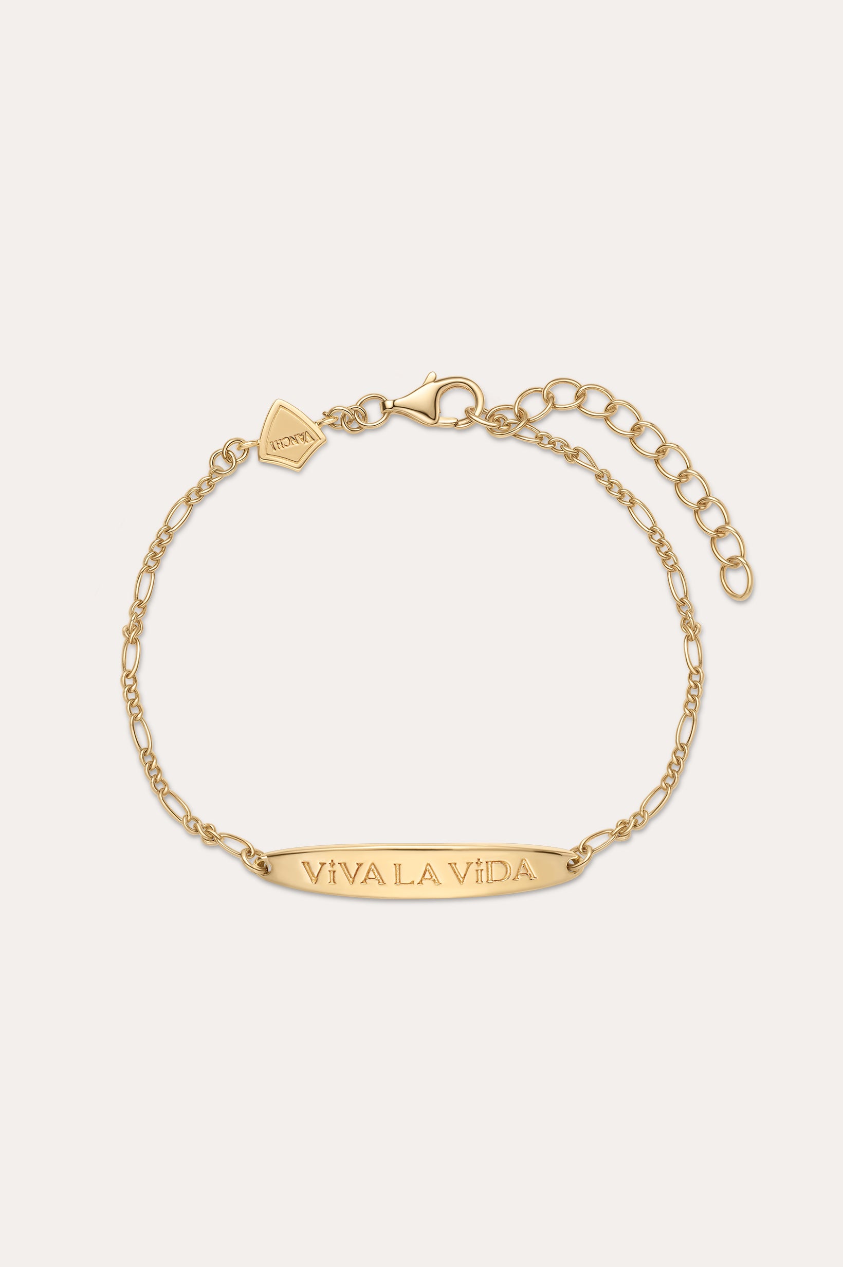 The Viva La Vida Bar Chain Bracelet in Gold features an adjustable clasp, a rectangular plate engraved with VIVA LA VIDA, and a small hexagonal charm near the clasp. Inspired by the classic Viva La Vida necklace; shown on a light beige background.