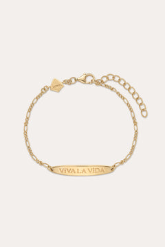 The Viva La Vida Bar Chain Bracelet in Gold features an adjustable clasp, a rectangular plate engraved with VIVA LA VIDA, and a small hexagonal charm near the clasp. Inspired by the classic Viva La Vida necklace; shown on a light beige background.